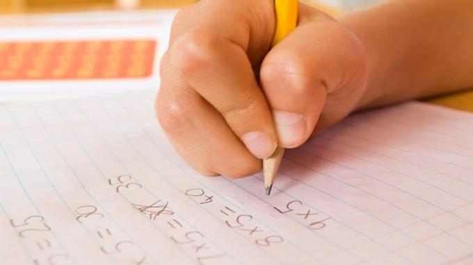 De hand van een kind die een huiswerkopdracht uitvoert met behulp van wiskundige aanpassingen