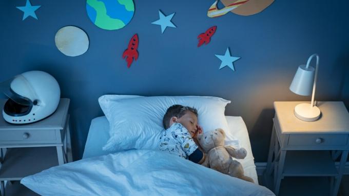 Hoge hoekmening van een kleine adhd-jongen die ervan droomt astronaut te worden terwijl hij slaapt met een teddybeer in een in de ruimte ingerichte kamer.